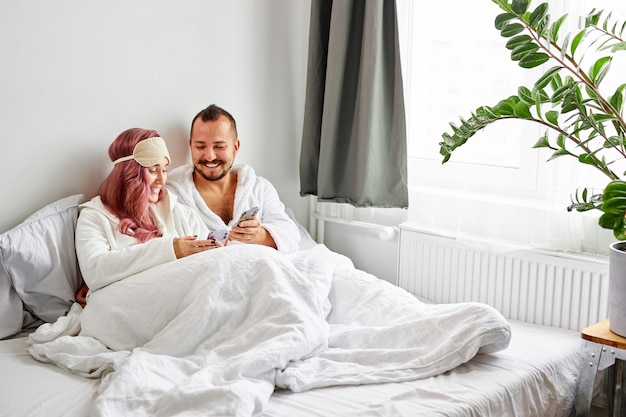 Relaxed couple use mobile phone lying on bed together