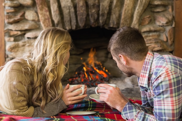 Relaxed couple with tea cups looking at lit fireplace