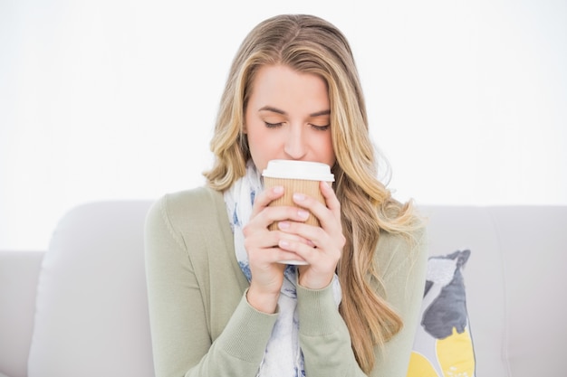 Relaxed cute blonde drinking coffee sitting on cosy sofa