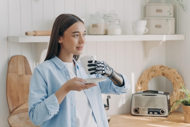 Relaxed disabled girl holds cup of coffee using bionic prosthetic arm enjoy daily routine at home