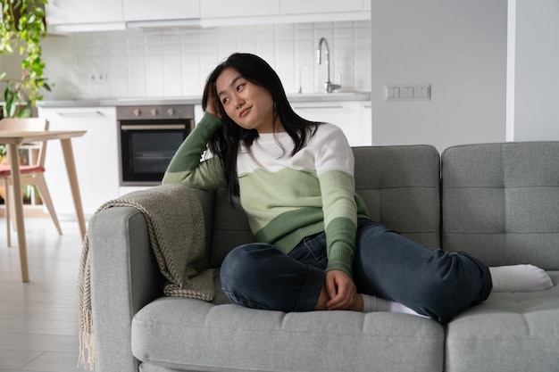 写真 ゆっくりとした夢想的なアジア人女性が自宅のソファに座って落ち着いたリラックスした週末を楽しんでいます