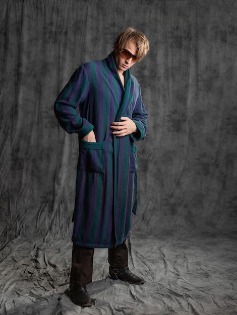 Relaxed dude after a party in a housecoat with a shaggy head posing in the studio on a gray backgrou