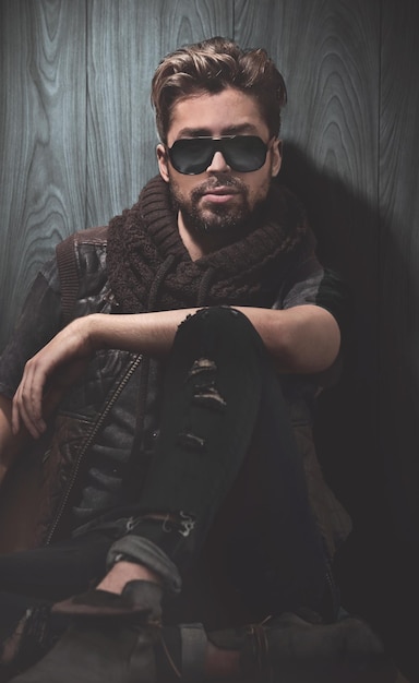 Relaxed fashion man in sunglasses sits on wood in studio