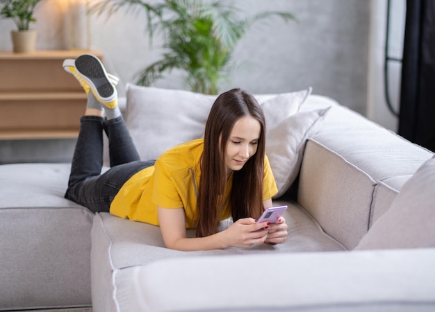 Relaxed freelancer woman SMM specialist web programmer housewife student businesswoman girl woman sitting on couch at home typing smartphone working remote distant job