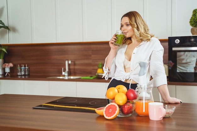 Relaxed girl being in the kitchen and drinking green smoothie