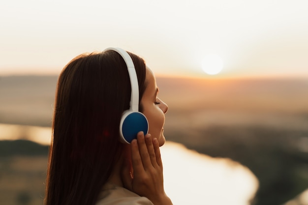 Photo relaxed girl listening to music wearing headphones at sunset. port