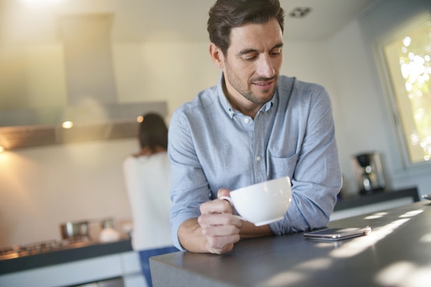  Relaxed handsome man in modern kitchen with wife in the background                              