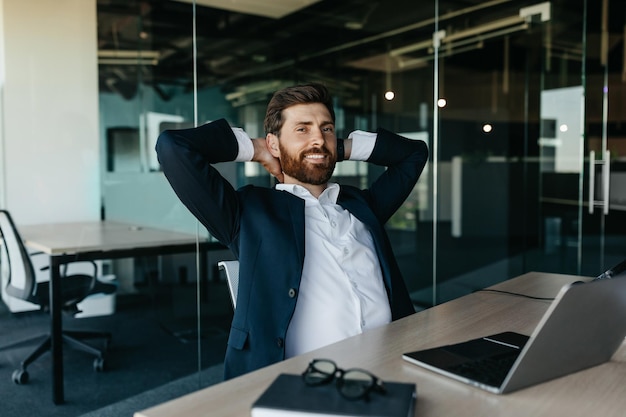 Relaxed happy businessman sitting at workplace in office leaning back on chair and smiling free space