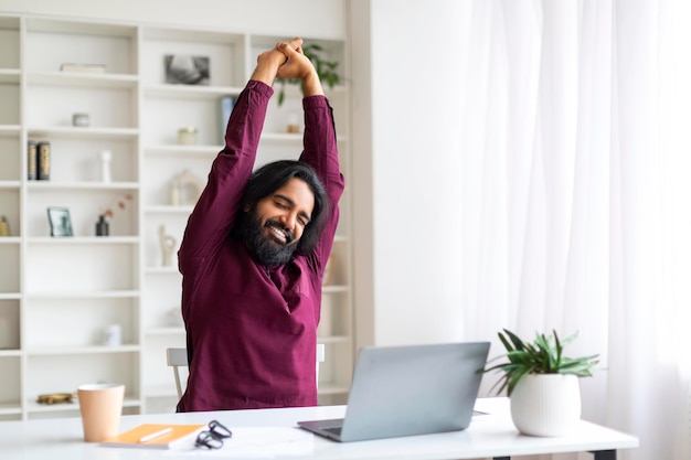 Photo relaxed indian freelancer man taking break and stretching after working on laptop