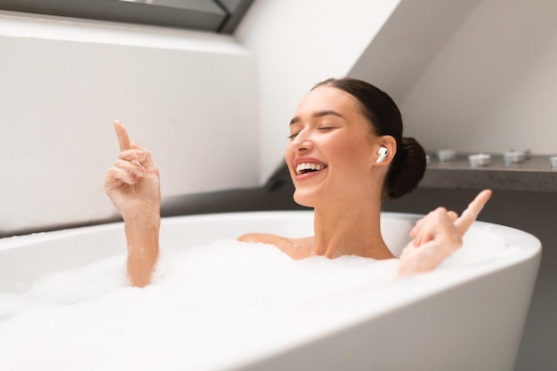 Relaxed lady with earbuds listening to music taking bath indoors