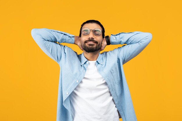 Relaxed man in a blue denim shirt hands behind head eyes closed smiling peacefully