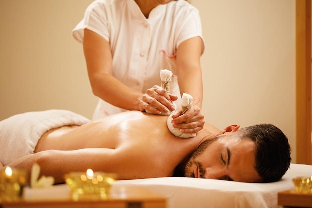 Relaxed man enjoying in back massage with herbal compress\
during spa treatment