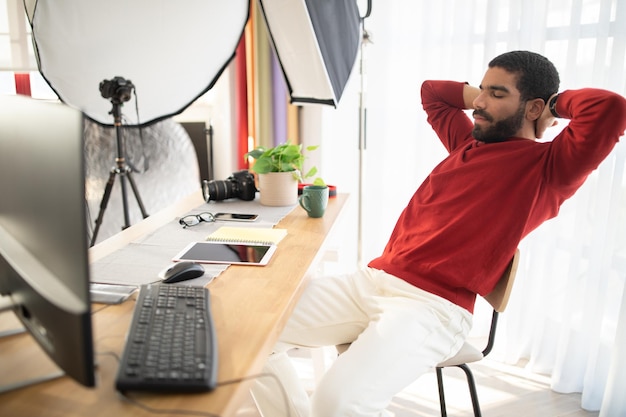 Foto fotografo uomo rilassato seduto alla scrivania in studio fotografico