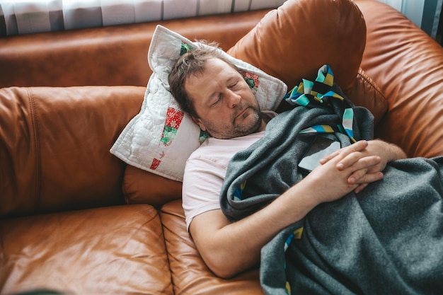 Relaxed man resting on a couch at home a tired husband dad
sleeps under a blanket on the sofa