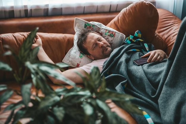 Photo relaxed man resting on a couch at home a tired husband dad sleeps under a blanket on the sofa