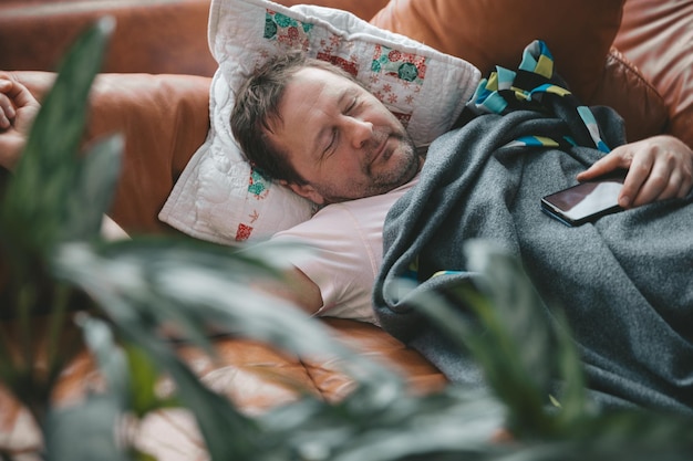 Relaxed man resting on a couch at home a tired husband dad
sleeps under a blanket on the sofa