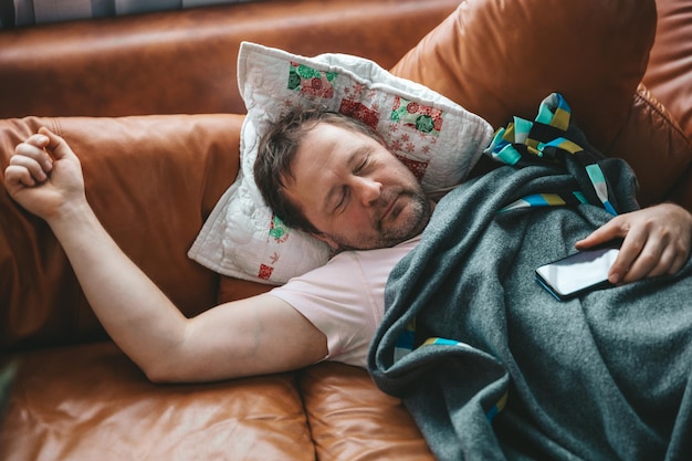 Relaxed man resting on a couch at home A tired Husband Dad sleeps under a blanket on the sofa