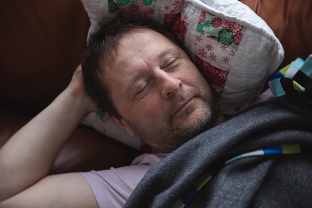 Relaxed man resting on a couch at home a tired husband dad\
sleeps under a blanket on the sofa