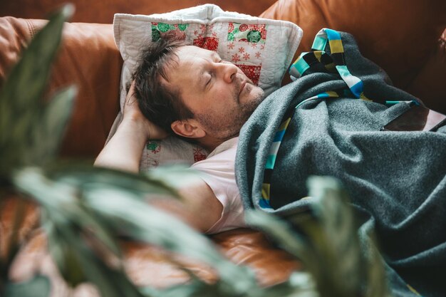 Relaxed man resting on a couch at home a tired husband dad
sleeps under a blanket on the sofa