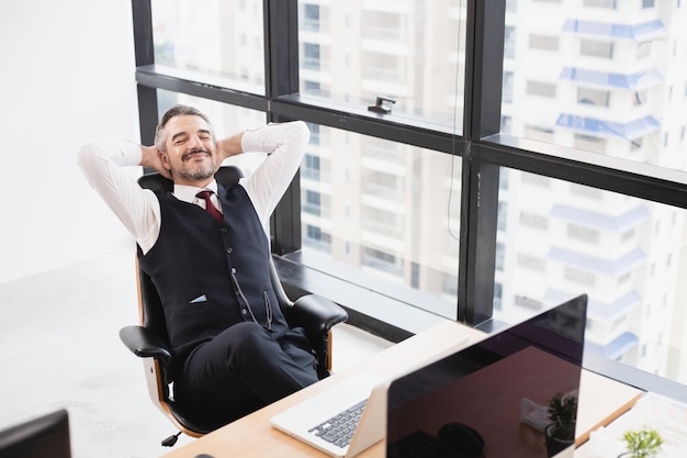 Расслабленный мужчина отдыхает от работы, заложив руки за голову, опираясь на удобное кресло в офисе.