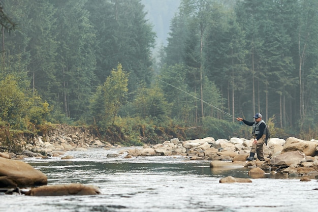 Relaxed man wearing special clothing while fishing on rough river among beautiful mountains. Concept of fishery and leisure time on nature.