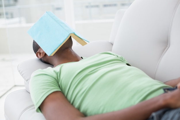 Relaxed man with book over face lying on sofa