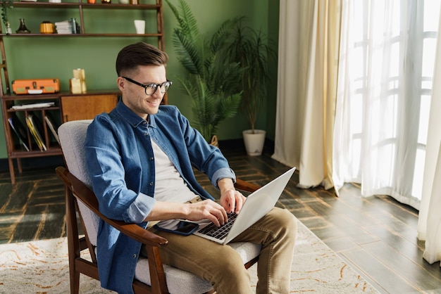 A relaxed man works on his laptop in a vintage chair surrounded by the calming influence of lush