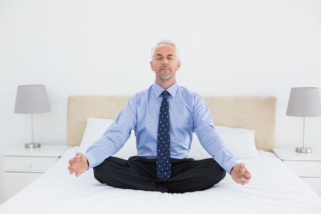 Relaxed mature businessman sitting in lotus posture on bed