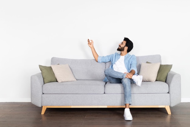 Relaxed middle eastern guy chilling on couch turning on ac