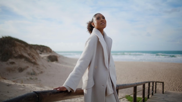 Relaxed model lean wooden pier at ocean shore serene african woman enjoy breeze