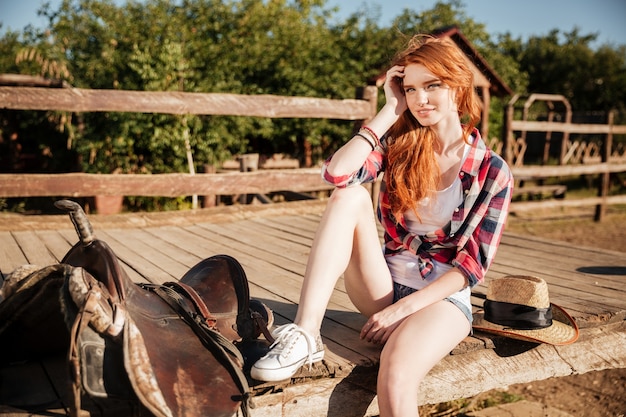 Photo relaxed redhead young woman cowgirl sitting and resting on ranch