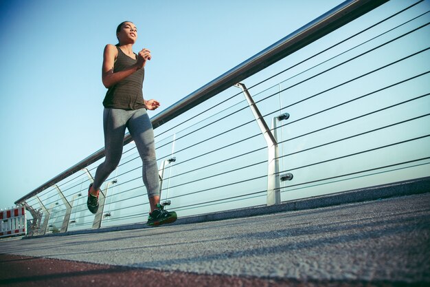 Relaxed sportswoman jogging on the bridge by the banister