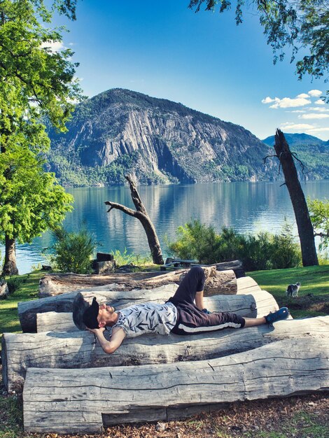 Фото Расслабленный турист отдыхает в отпуске на бревнах перед озером с горами