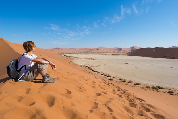 Relaxed tourist sitting on sand dunes and looking at the stunning view in Sossusvlei, Namib desert, Namibia, Africa