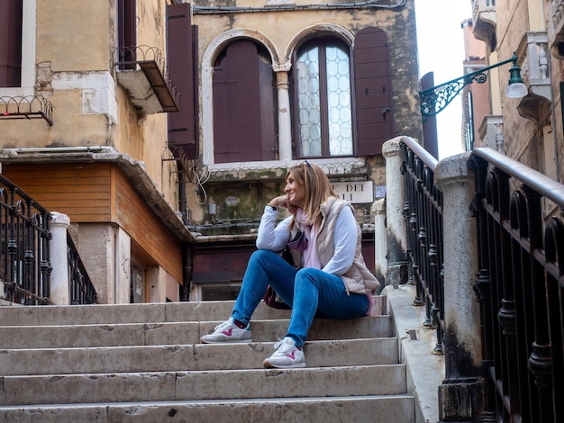 イタリア、ベニスの街の橋の上の階段に座っているリラックスした観光客の女性