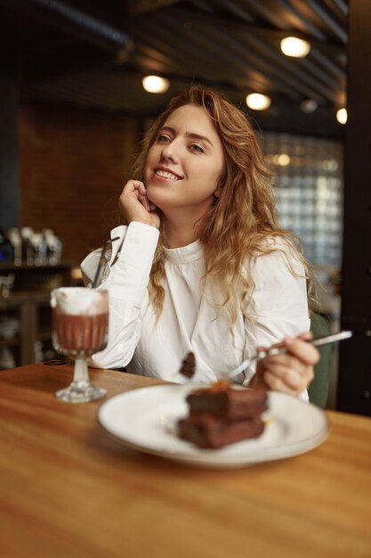 Relaxed woman in casual clothes sitting at table with chocolate cake and hot fresh cocoa