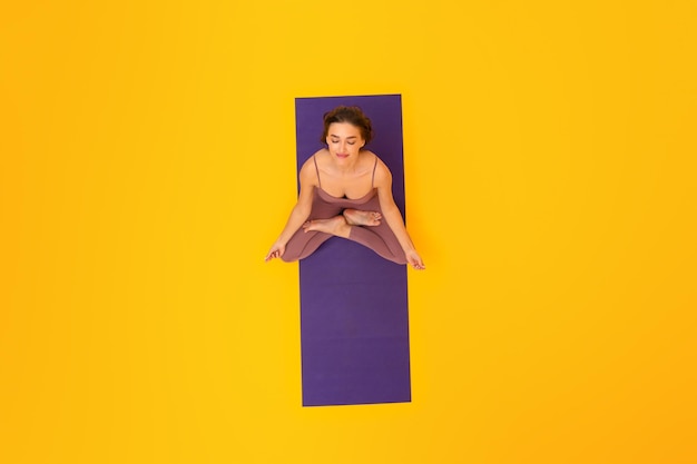 Relaxed woman doing yoga sitting in lotus pose yellow background