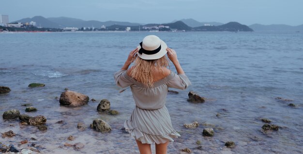 바람이 부는 흐린 날씨에 아름다운 해변 해안선에서 바다 만, 자유와 생활을 즐기는 편안한 여자. 자유롭고 편안하며 행복하다고 느끼는 젊은 아가씨. 휴가, 자유, 행복, 즐거움의 개념