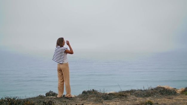 Photo relaxed woman enjoying ocean landscape rear view carefree girl stretching cliff