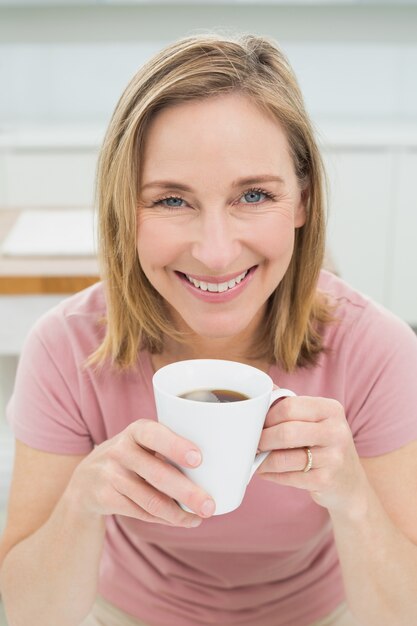 キッチンにコーヒーを持っているリラックスした女性