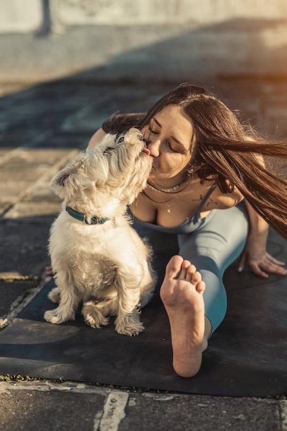 Relaxed woman playing with her dog pets while practicing yoga stretching exercise on a rooftop terrace.