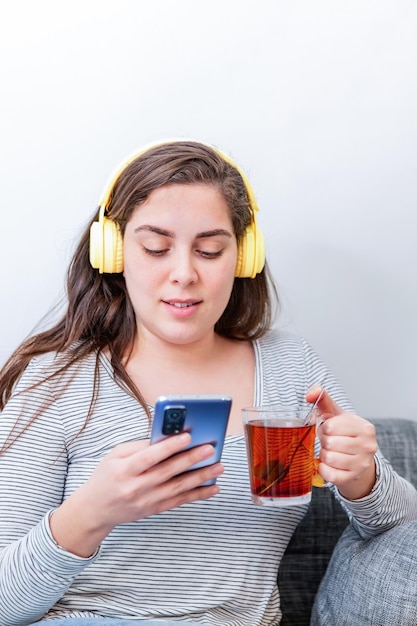 Relaxed woman with headphones watching video on smart phone sitting on a couch in the living room at home