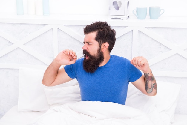 Relaxed yawning man waking up in the morning in bed at home lazy sunday