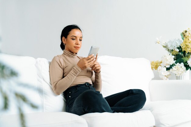 Photo relaxed young african american woman using crucial mobile phone on sofa couch