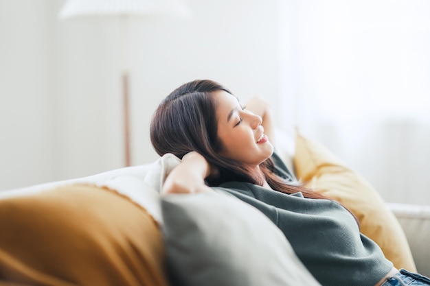 Photo relaxed young asian woman enjoying rest on comfortable sofa at home