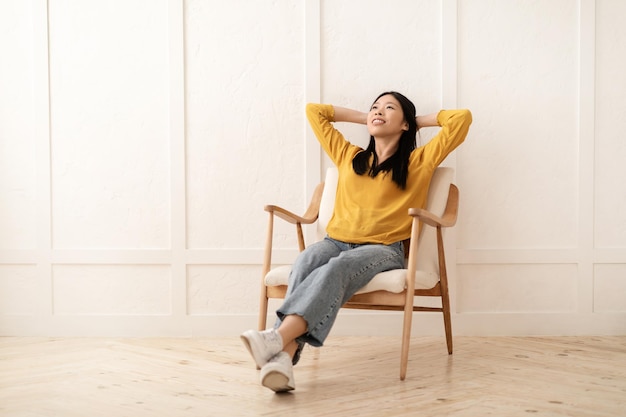 Relaxed young asian woman relaxing in armchair at home