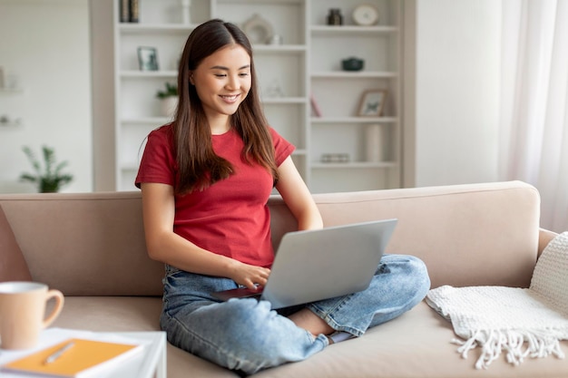 Relaxed young asian woman smiling while browsing on her laptop