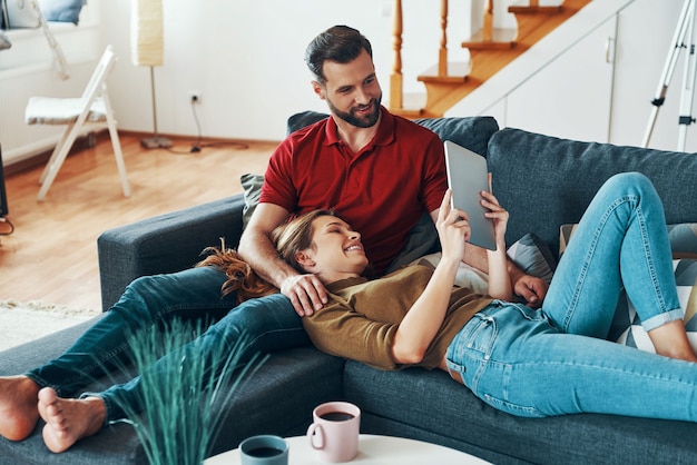 Relaxed young couple in casual clothing bonding together and smiling while resting on the sofa indoors