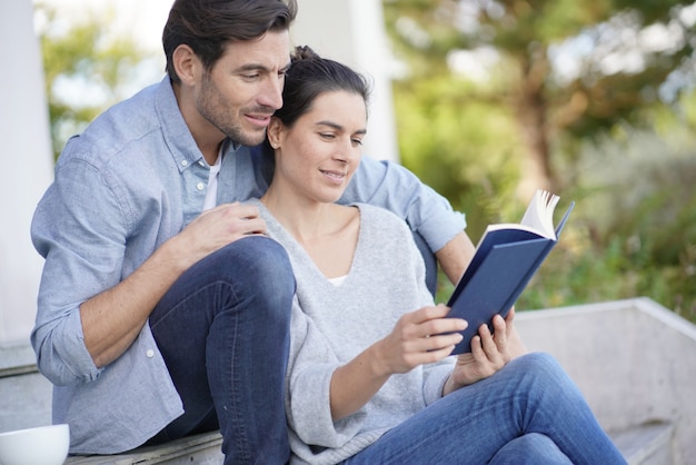 リラックスした若いカップルの外で一緒に座っていると読書