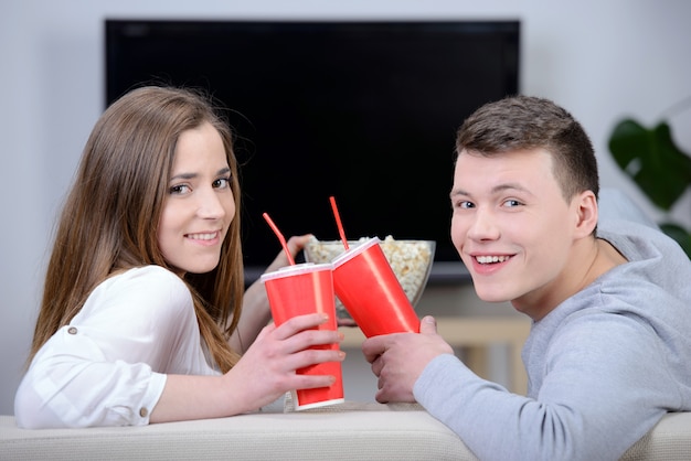 Relaxed young couple watching tv and drinking soda.